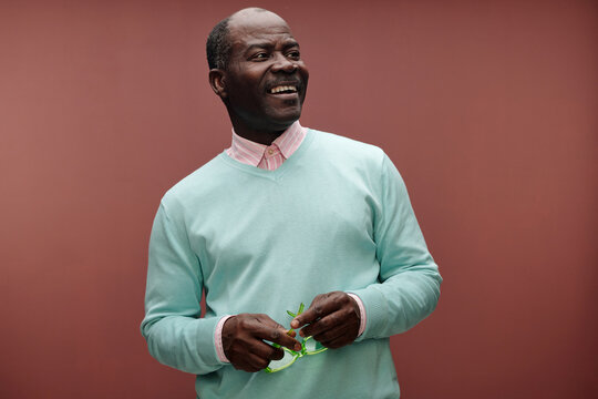 Smiling Elderly Man Holding Green Glasses Against Brown Background