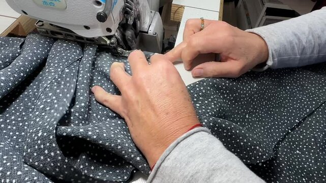 The process of sewing a dress. A seamstress uses an overlock machine to sew dress, guiding the fabric with both hands. The overlock machine sews and finishes the edge of the fabric.
