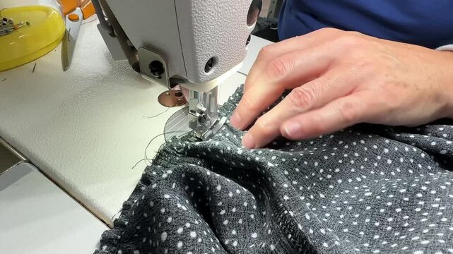 The process of sewing a dress. Close-up hands a seamstress guiding fabric through an industrial sewing machine, creating elegant pleats in a stylish dress.