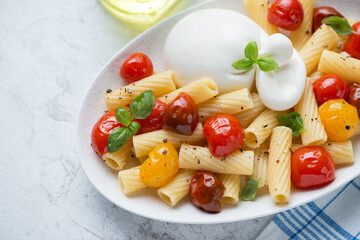 Tortiglioni pasta served with roasted cherry tomatoes, burrata cheese and basil, horizontal shot, selective focus, middle close-up