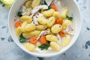 Bowl of creamy soup with chicken fillet and potato gnocchi on a white and blue granite surface, horizontal shot, middle close-up