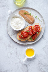 Roasted tomato bruschettas and stracciatella cheese, vertical shot on a white stone background with space, top view