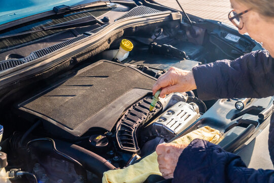 An elderly woman checks the oil level in her car by pulling out the dipstick from the engine. 