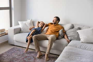Mature dad and his little daughter settled down comfortable lying on couch in modern, well-lit...