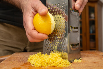 Male chef hands grating a lemon fruit on a stainless steel grater, for lemon zest seasoning, soft...