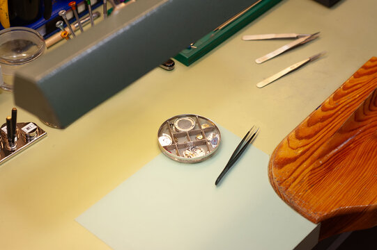 Mesa de trabajo de un relojero: pinzas y distintas piezas del movimiento de un reloj de mu&ntilde;eca desmontado sobre una mesa de trabajo.