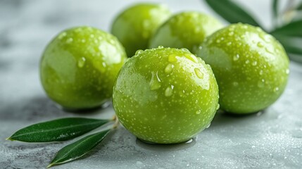 Fresh green olives with water droplets on a light gray surface with olive leaves