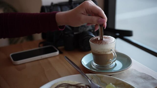 Chica joven con pelo largo tomando caf&eacute; y tortitas en cafeter&iacute;a estilo cozy