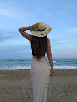Mujer de espaldas en atardecer en la playa con un sombrero que pone "no molestar"