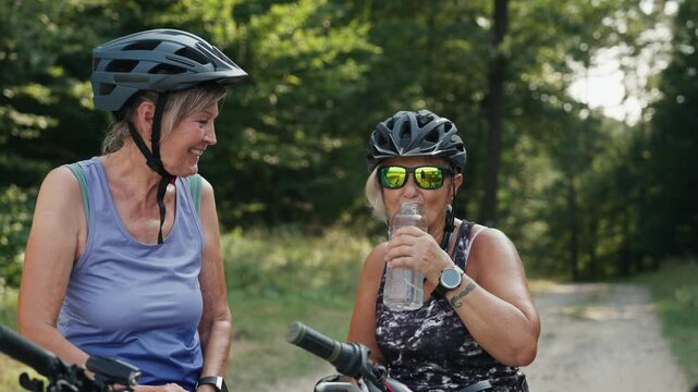 Senior friends on bike tour in nature resting, drinking water. Older women on low impact route riding electric bikes.