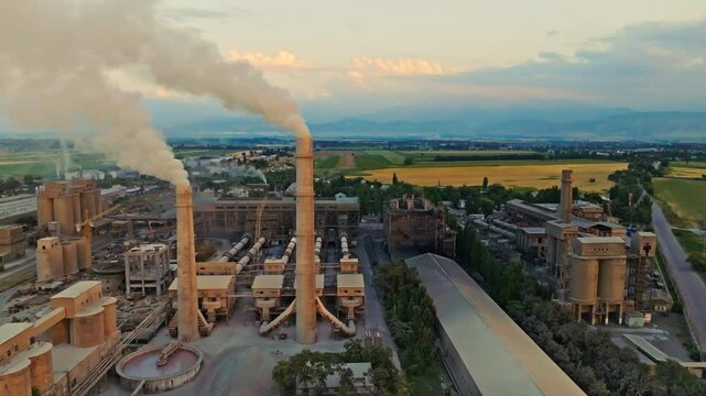 aerial view of two smoking pipes of soviet concrete factory at summer sunset