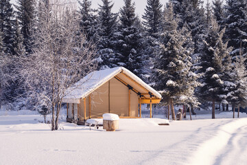 A Cozy Winter Cabin That is Gently Surrounded by Beautiful, Snowy Trees in the Landscape. A charming wooden cabin is snugly nestled in deep white snow, surrounded by tall evergreens under a clear