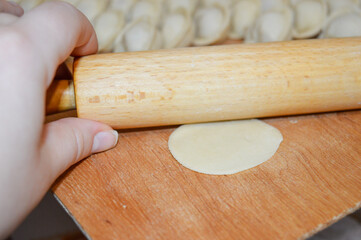 close-up of a hand rolling out dough with a wooden rolling pin on a wooden surface dumplings pelmeni in rows cooking homemade food traditions preparation recipes tutorials cuisine family