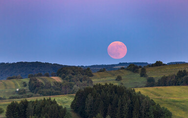 the moon rising over the hills