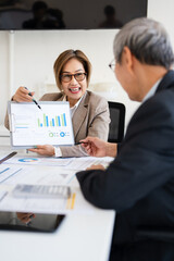 senior professionals work on a project in modern office, analyzing documents and charts. The man focuses intently the woman reviews papers, dynamic scene of collaboration and expertise.