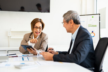 Female executive assistant holding a tablet as she shows her boss a business report indicating the company's growth and success. Happy  business woman working with a mature male professional
