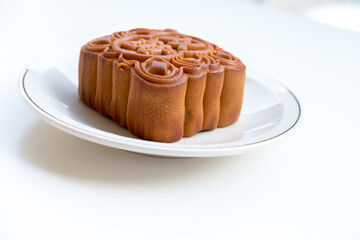 Mooncake on a white plate with silver rim, side-angle shot. Bright lighting shows texture and detail of the crust.