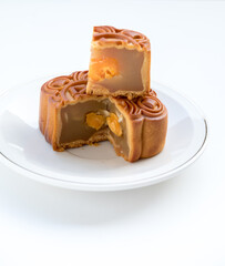 Mooncake with stacked slices showing filling and double egg yolks. Angled shot on a white plate. Bright lighting shows intricate details