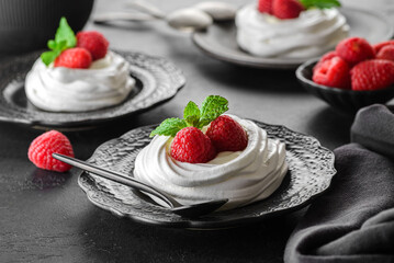 pavlova meringue dessert with raspberries and cream on a black background