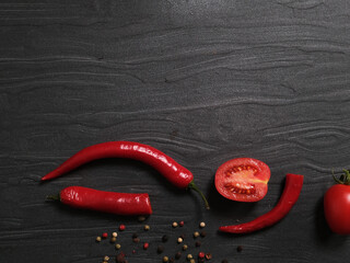 Peperoncino e pomodoro tagliati con grani di pepe su piano in pietra nera, spazio per testo, 