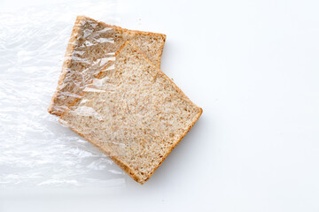 Whole wheat bread slices. Fresh, healthy food. Plastic wrap, simple shot. Top-down view, white background.
