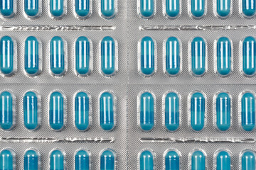 A close-up, overhead shot of multiple blister packs filled with blue capsules highlights their pharmaceutical packaging and medical purpose