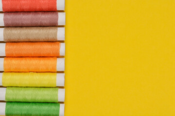 A top-down shot of a row of colorful spools of thread arranged vertically against a solid yellow background, showcasing their vibrant hues and textures