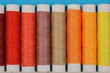 A close-up, horizontal shot of a row of colorful spools of thread arranged against a blue background, showcasing their vibrant hues and textures