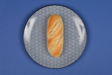A top-down shot of a plain white bread roll with diagonal cuts, centered on an oval plate with a...