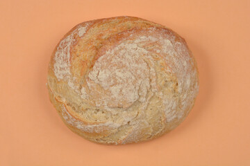 A top-down view of a round, rustic loaf of bread dusted with flour, presented on a solid peach-colored background