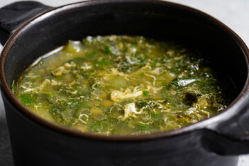 Soup with green sorrel in black ceramic pot on gray background