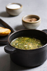 Soup with green sorrel in black ceramic pot on gray background