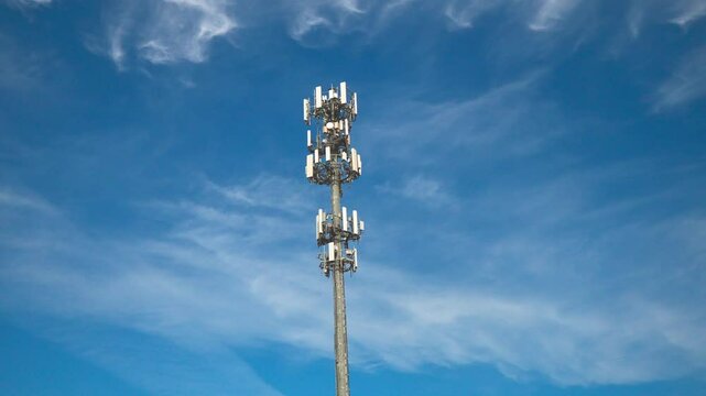 Rising tilting upward shot of a  cellular communications tower and antenna providing digital service in a shopping area on a sunny day with clouds.