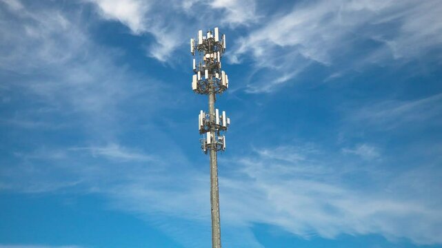 Zoom out shot of a cellular communications tower and antenna providing digital service on a sunny day with moving clouds.