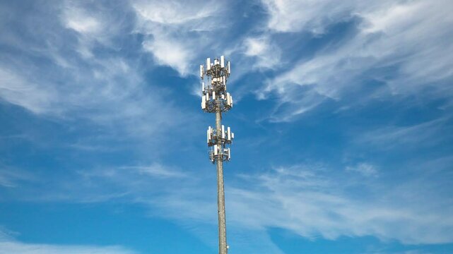 Static shot of a cellular communications tower and antenna on a sunny day with moving clouds.