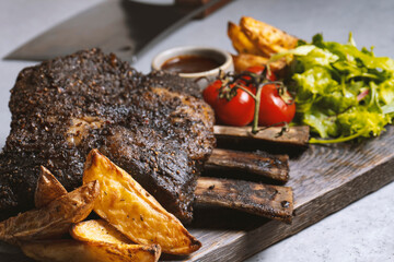 grilled pork ribs with french fries and vegetables on a wooden board