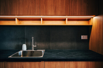 Water faucet and metallic sink in modern sleek kitchen with led strip light