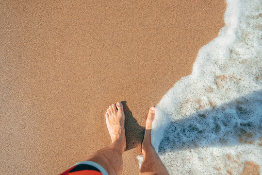 First person point of view of wet feet on sandy beach during summer vacation