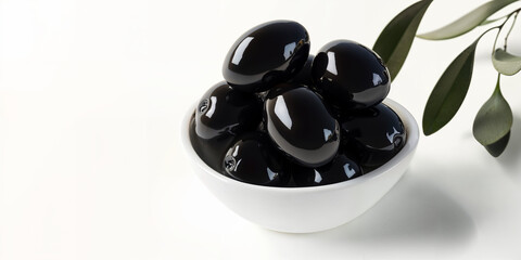 Glossy black olives arranged in a white bowl with greenery on a light surface