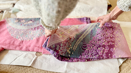 ピンク色の振り袖をたとう紙の上でたたむ高齢女性の両手