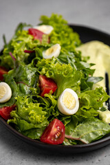 Fresh green salad with quail eggs, cherry tomatoes and guacamole in black plate on grey background