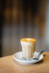 Side view of hot latte coffee with latte art in a glass on wooden table at coffee shop, copy space concept.