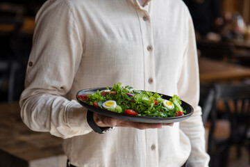 Close-up of a man holding a bowl of salad with eggs and cherry tomatoes. Waiter