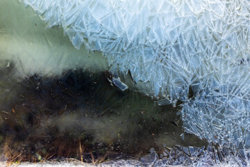 Abstract frozen water surface with intricate ice patterns. A close-up of a partially frozen surface showcasing sharp ice formations and dark water below. 