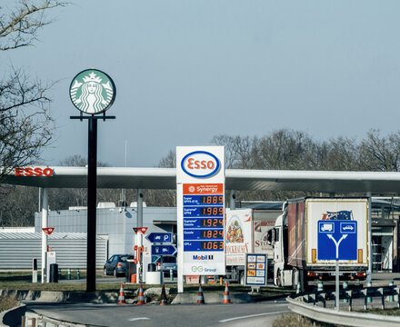 Haguenau, France - Feb 18, 2025: A highway Esso gas station with a Starbucks sign, fuel price board, multiple fuel pumps, trucks refueling, and traffic signs under a clear sky during the daytime