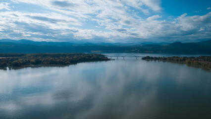Aerial view of a bridge spanning a wide river, connecting two lush green landscapes.