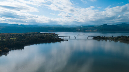 Aerial view of a bridge spanning a wide river, connecting two lush green landscapes.