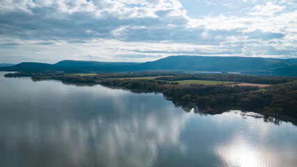 Obraz premium Aerial view of a vast lake reflecting clouds, surrounded by rolling hills and distant mountains.