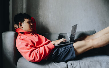Young Person in Bright Hoodie Working on Laptop while Relaxing at Home on a Couch © IgnatiusHarly