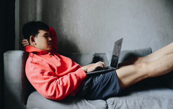 Young Person in Bright Hoodie Working on Laptop while Relaxing at Home on a Couch